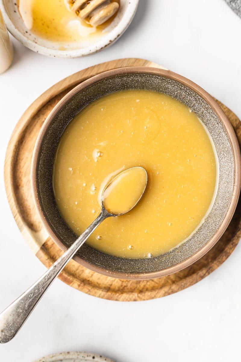 Cremige, goldene Honig-Senf-Sauce in einer kleinen Schale, umgeben von geschnittenem Gemüse wie Karotten und Gurken.