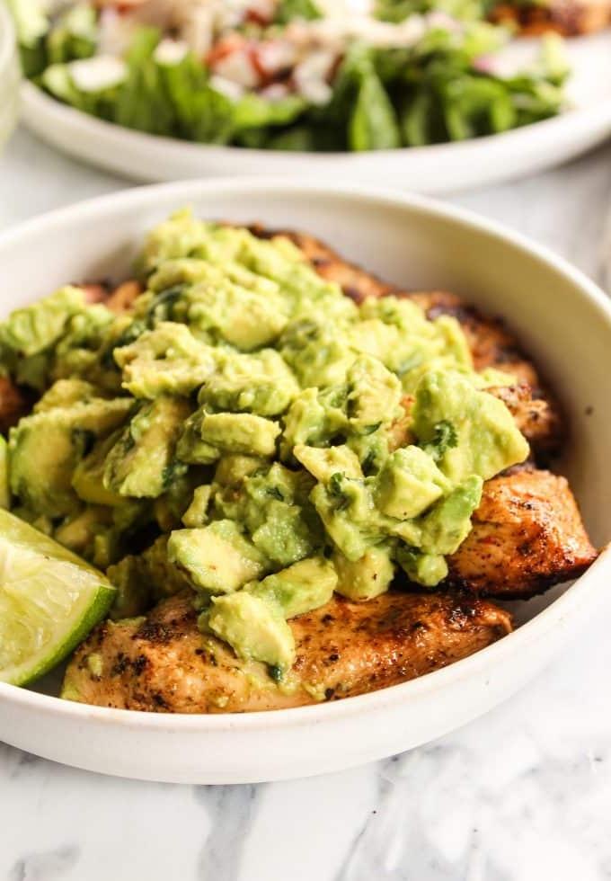 Gegrilltes Hähnchen mit Avocado-Topping auf einem Teller angerichtet, garniert mit frischem Koriander.