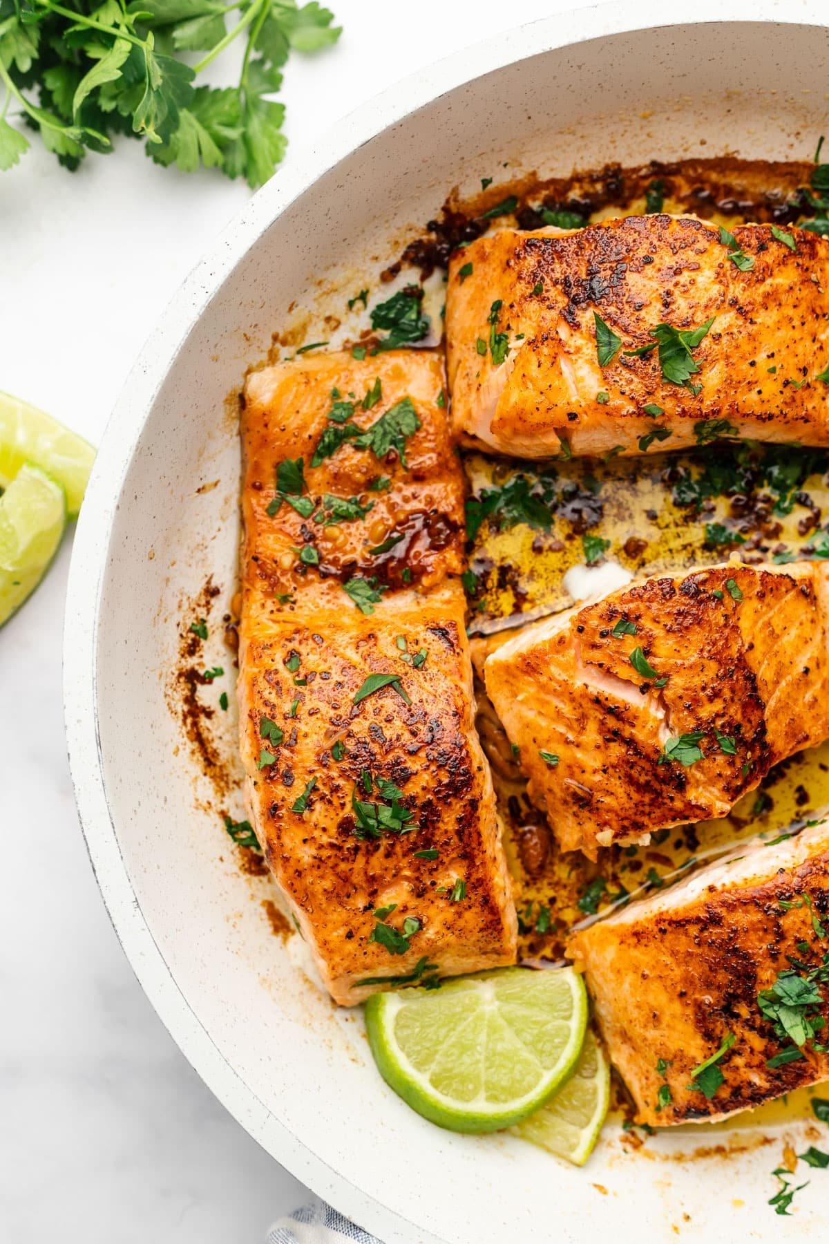 Einfacher scharf angebratener Chipotle-Limetten-Lachs 2 Frisch gebratener Lachs mit Limettenscheiben und Petersilie in einer Pfanne.