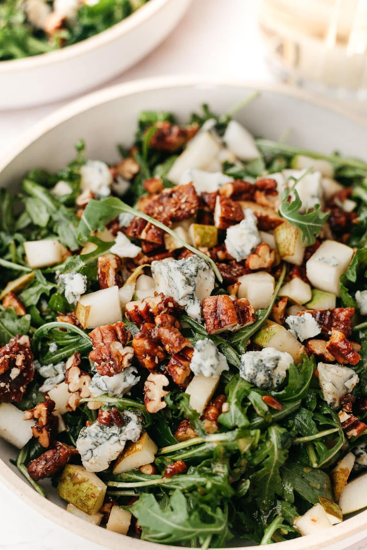 Rucola-Birnen-Salat mit karamellisierten Pekannüssen 2 Rucola-Birnen-Salat mit kandierten Pekannüssen und Gorgonzola auf einem rustikalen Teller angerichtet.