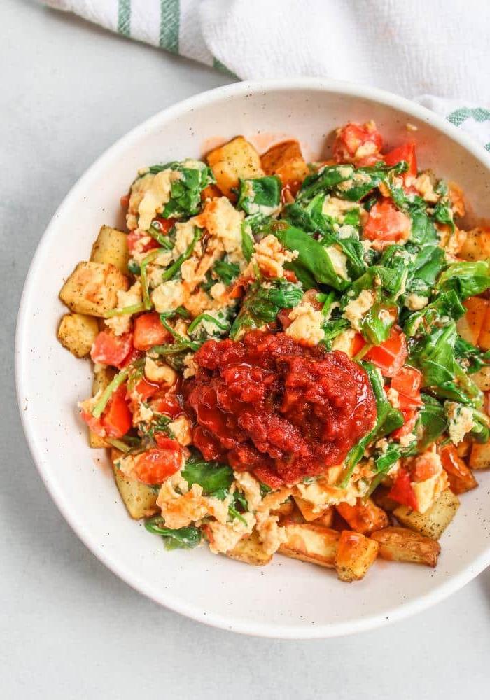 Rührei mit Heißluftfrittier-Kartoffeln 2 Ein Teller mit Rührei, Spinat und Tomaten, daneben knusprige Kartoffeln aus der Heißluftfritteuse, mit Salsa und frischen Kräutern garniert.