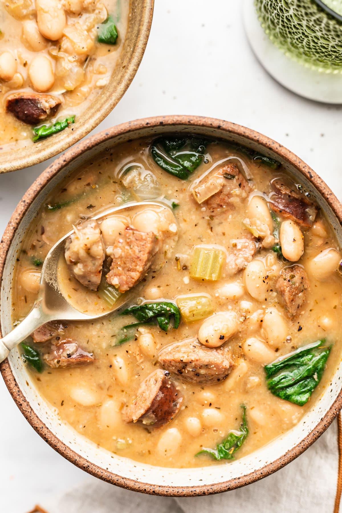Einfache Wurst- und Weiße-Bohnen-Suppe 2 Eine dampfende Schüssel cremige weiße Bohnensuppe mit Wurst, garniert mit frischen Kräutern