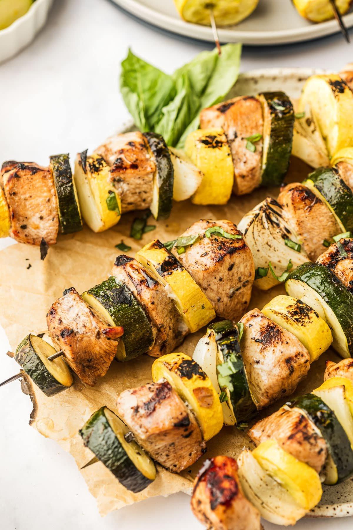 Gegrillte Hähnchenspieße mit Zucchini, Kürbis und Zwiebeln auf Holzspießen, appetitlich angerichtet.