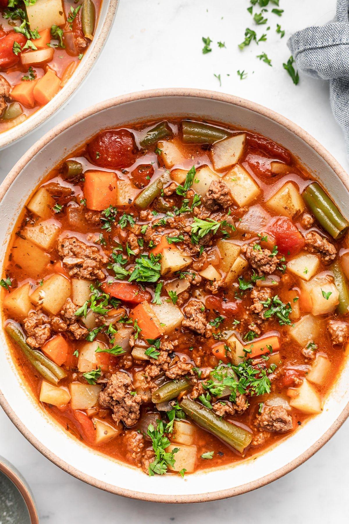 Gesunde 30-Minuten-Hamburger-Suppe 2 Eine dampfende Schüssel gesunde 30-Minuten-Hackfleischsuppe mit frischer Petersilie garniert, daneben ein knuspriges Stück Knoblauchbrot.