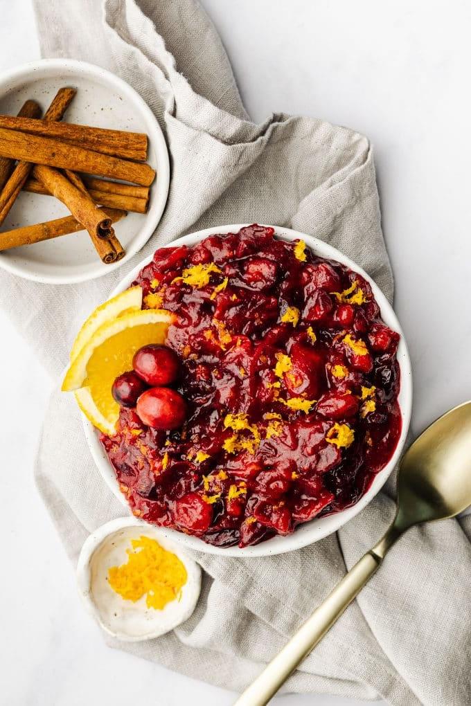 Frisch zubereitete Orangen-Preiselbeersauce in einer kleinen weißen Schale, umgeben von frischen Preiselbeeren und Orangenscheiben