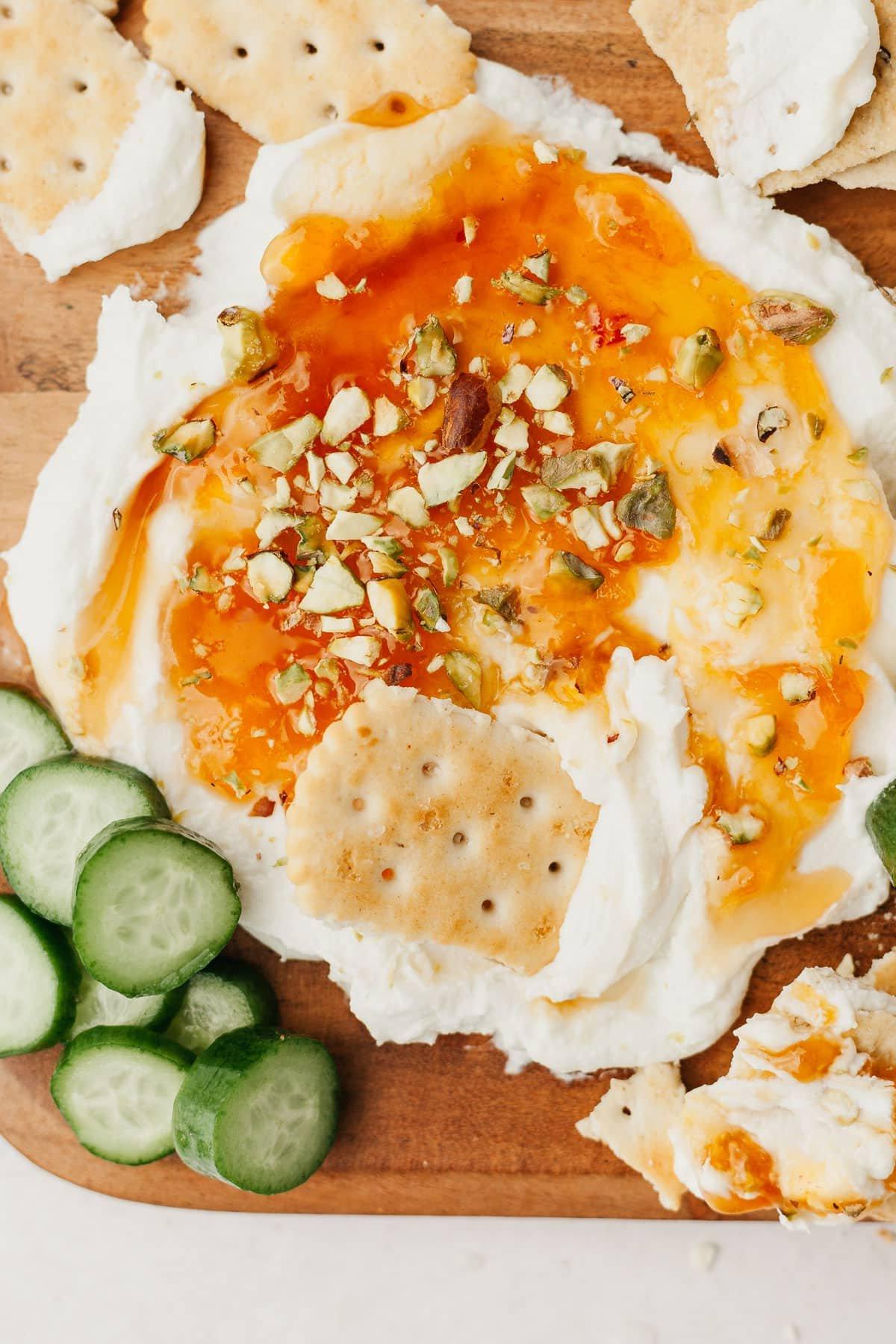 Cremiger Ziegenkäse-Aufstrich mit Aprikosenkonfitüre, scharfem Honig und gehackten Pistazien auf einem Holzbrett angerichtet, bereit zum Servieren und Genießen.