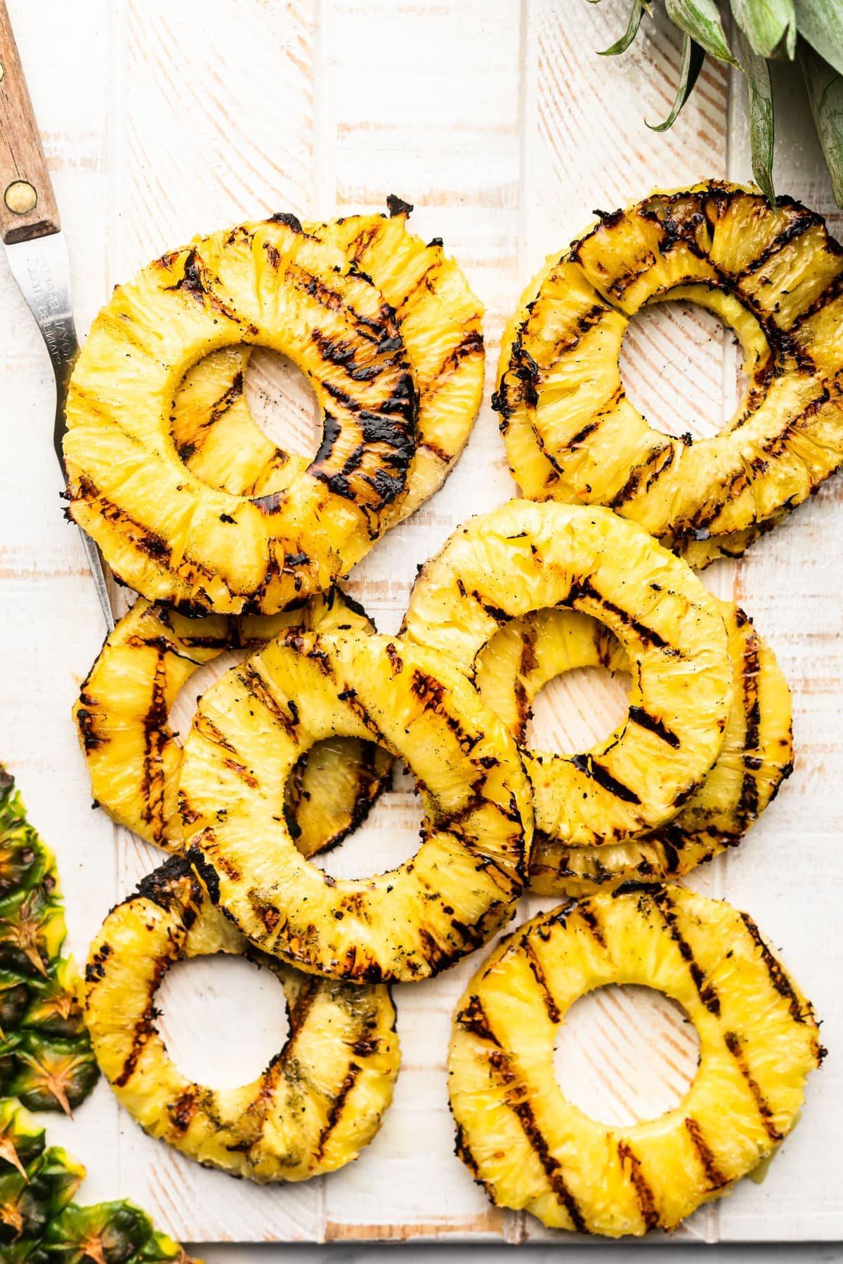 Frische Ananasringe auf dem Grillrost, leicht karamellisiert mit sichtbaren Grillstreifen.
