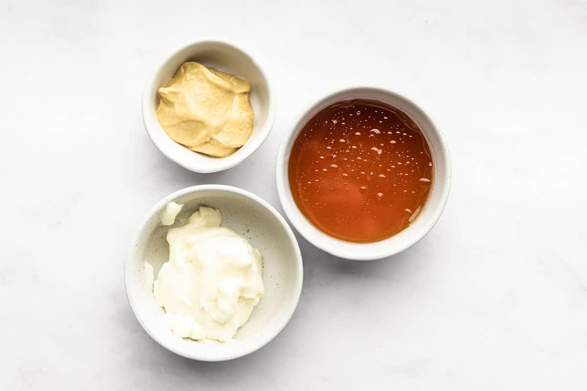 Cremige Honig-Senf-Sauce in einer weißen Schale mit einem Löffel daneben, der die glatte Textur der Sauce zeigt.