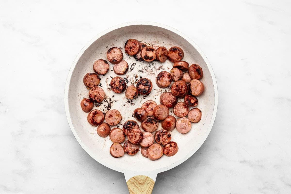 **20-Minuten-Wurst-Zucchini-Pfanne** 3 Zutaten für die Zucchini-Wurst-Pfanne, darunter geschnittene Wurst, Zucchini, Zwiebel und Paprika.