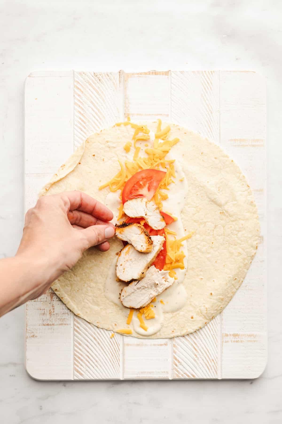 Gegrillte Ranch-Hähnchen-Wraps 3 Nahaufnahme eines halbierten Hähnchen-Ranch-Wraps, der die Füllung mit Hähnchen, Käse und Tomaten zeigt.