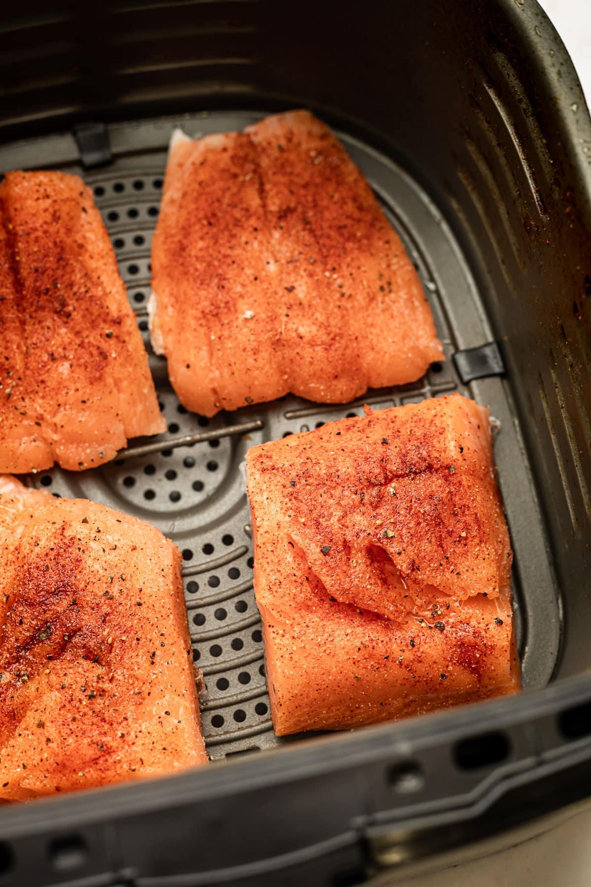 **Heißluftfritteusen-Lachs** 3 Drei frische, rohe Lachsfilets, appetitlich angerichtet auf einer sauberen Oberfläche, umgeben von einer kleinen Schale Olivenöl und einer Mischung aus verschiedenen Gewürzen, bereit zur Vorbereitung für die Heißluftfritteuse.