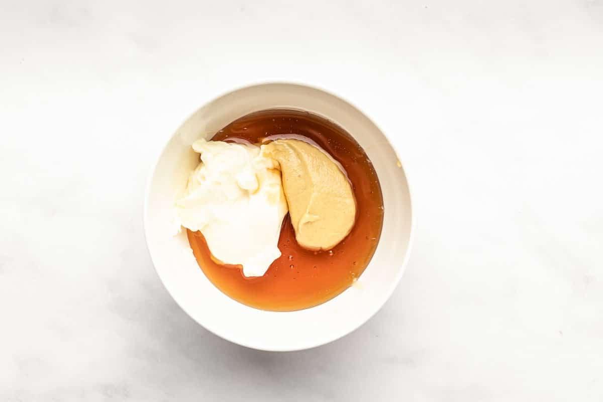 Eine Schüssel mit glatter Honig-Senf-Sauce auf einem Holztisch, im Hintergrund unscharf weitere Zutaten.