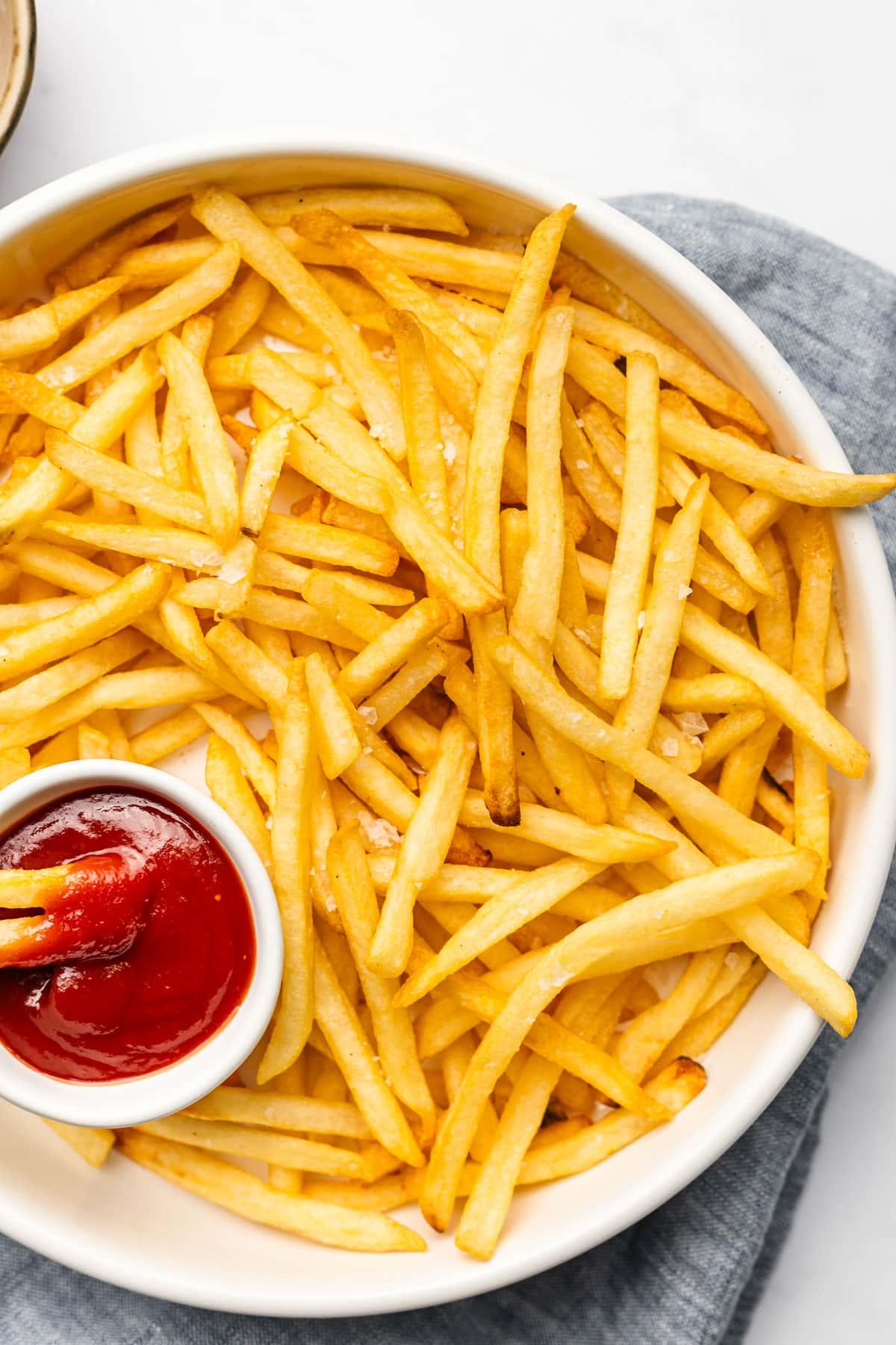 Tiefkühl-Pommes aus der Heißluftfritteuse 4 Fertig gebackene, knusprige Pommes aus der Heißluftfritteuse in einem Teller mit Saucen.