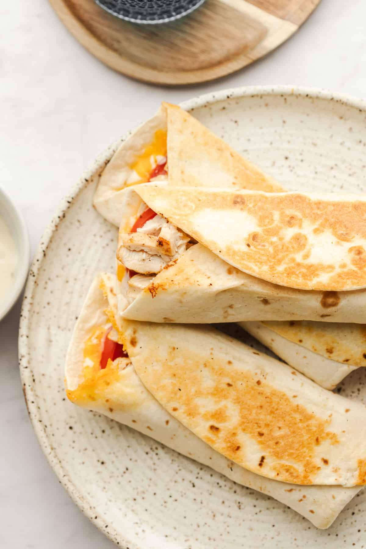 Gegrillte Ranch-Hähnchen-Wraps 4 Drei fertig gefaltete und gegrillte Hähnchen-Ranch-Wraps auf einem Gitterrost, leicht gebräunt.
