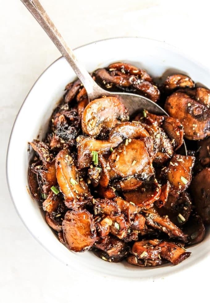 Gebratene Champignons mit Knoblauch 4 Drei Pfannen mit sautierten Knoblauch-Champignons auf einem Holztisch, bereit zum Servieren.