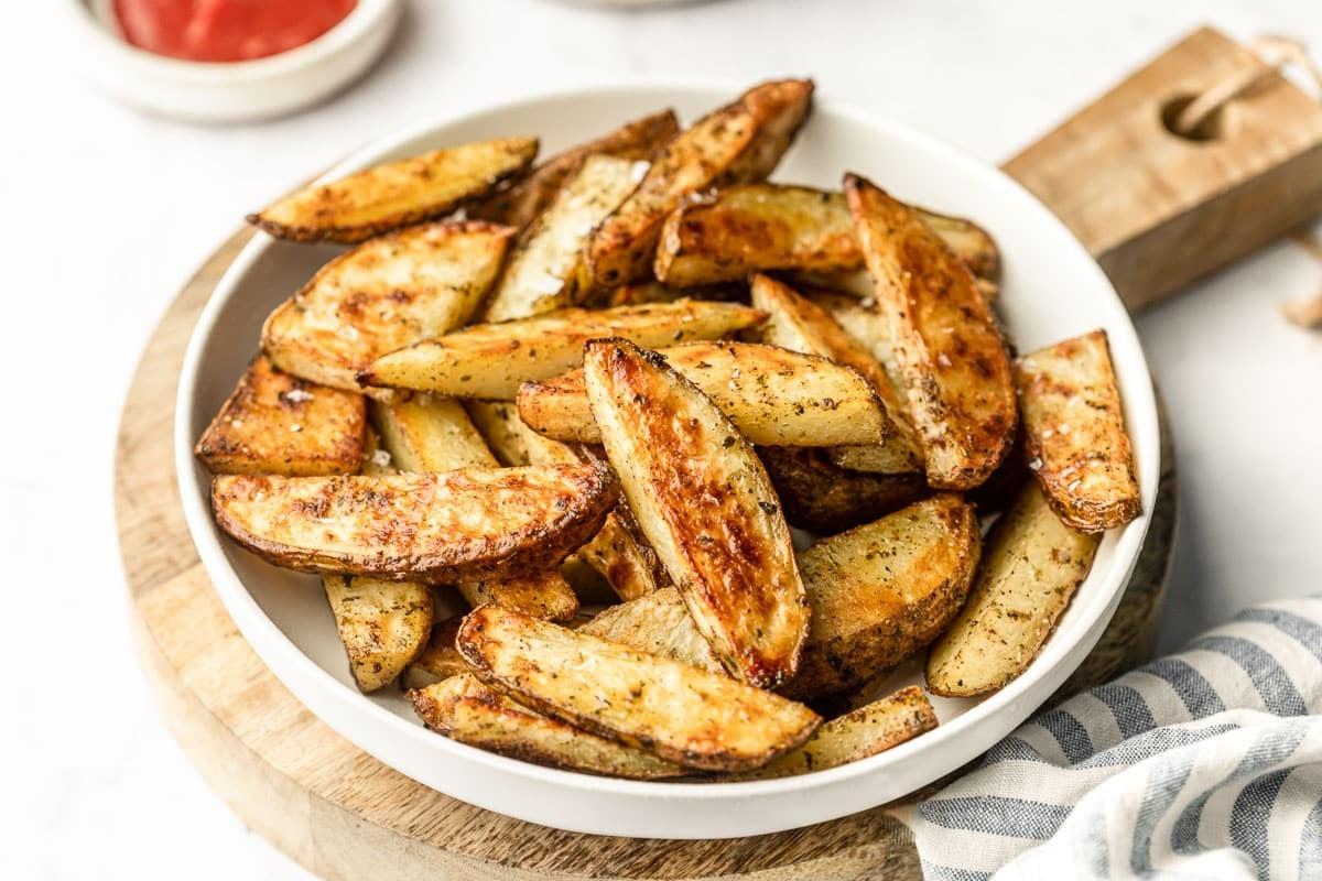 Servierfertige, knusprige Ofenkartoffelspalten in einer Schüssel mit Dip