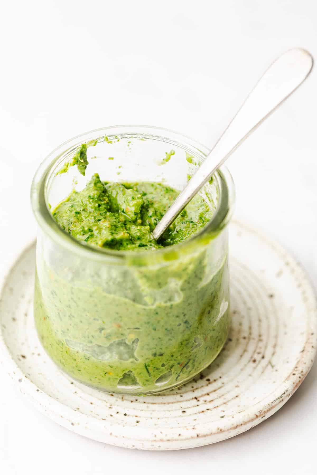 Pistazien-Zitronen-Pesto in einem kleinen Marmeladenglas, umgeben von frischen Basilikumblättern