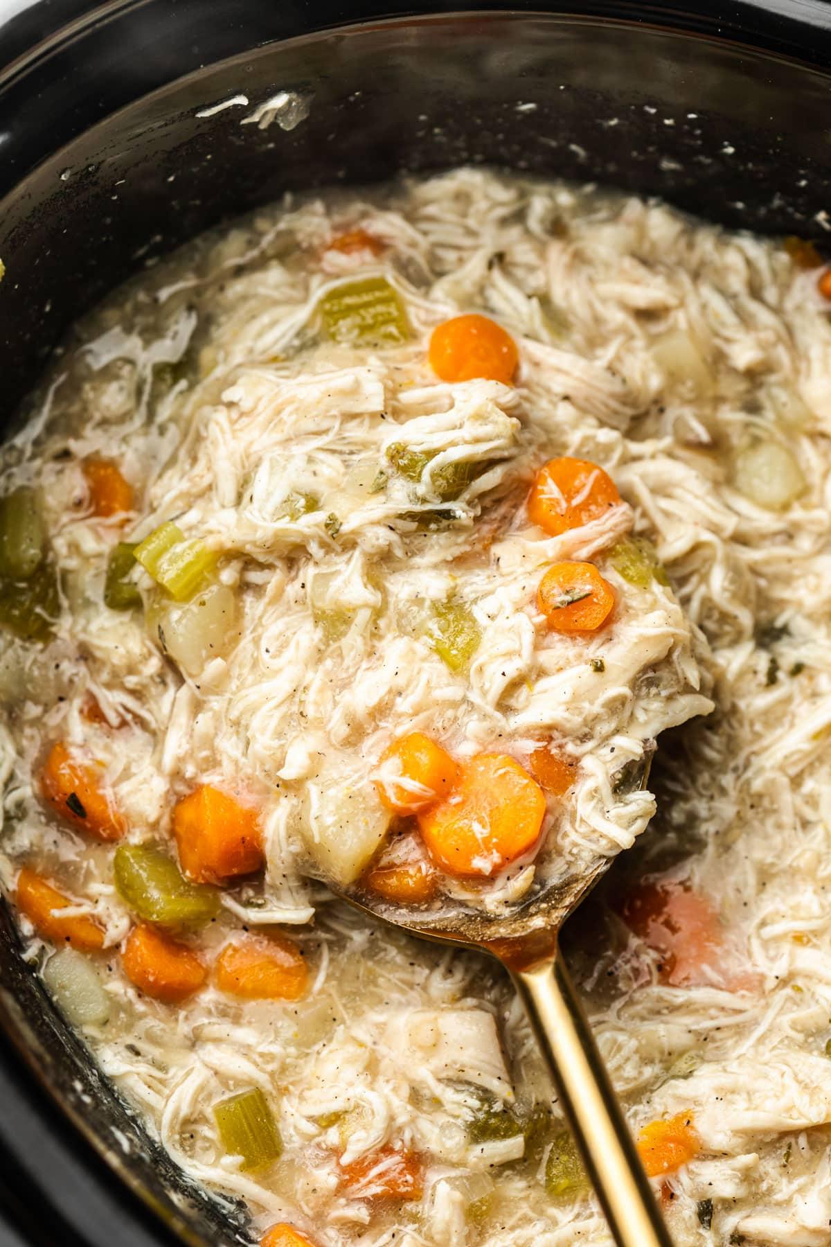 **Schongarer Herzhafter Hähncheneintopf** 5 Der Hähncheneintopf in einem Slow Cooker Topf mit einem Schöpflöffel, bereit zum Servieren.