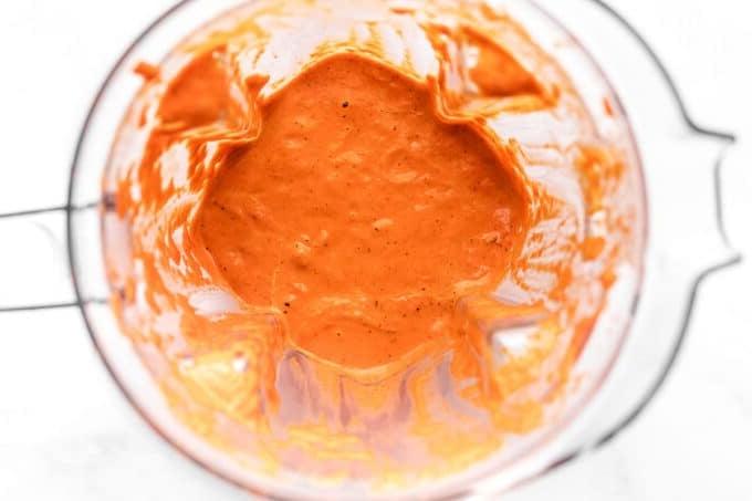 5-Minuten-cremige geröstete rote Paprika-Soße 5 Geröstete Paprikasauce in einer Schüssel mit einem Löffel, daneben frischer Basilikum und Knoblauchzehen, die Zutaten andeutend.