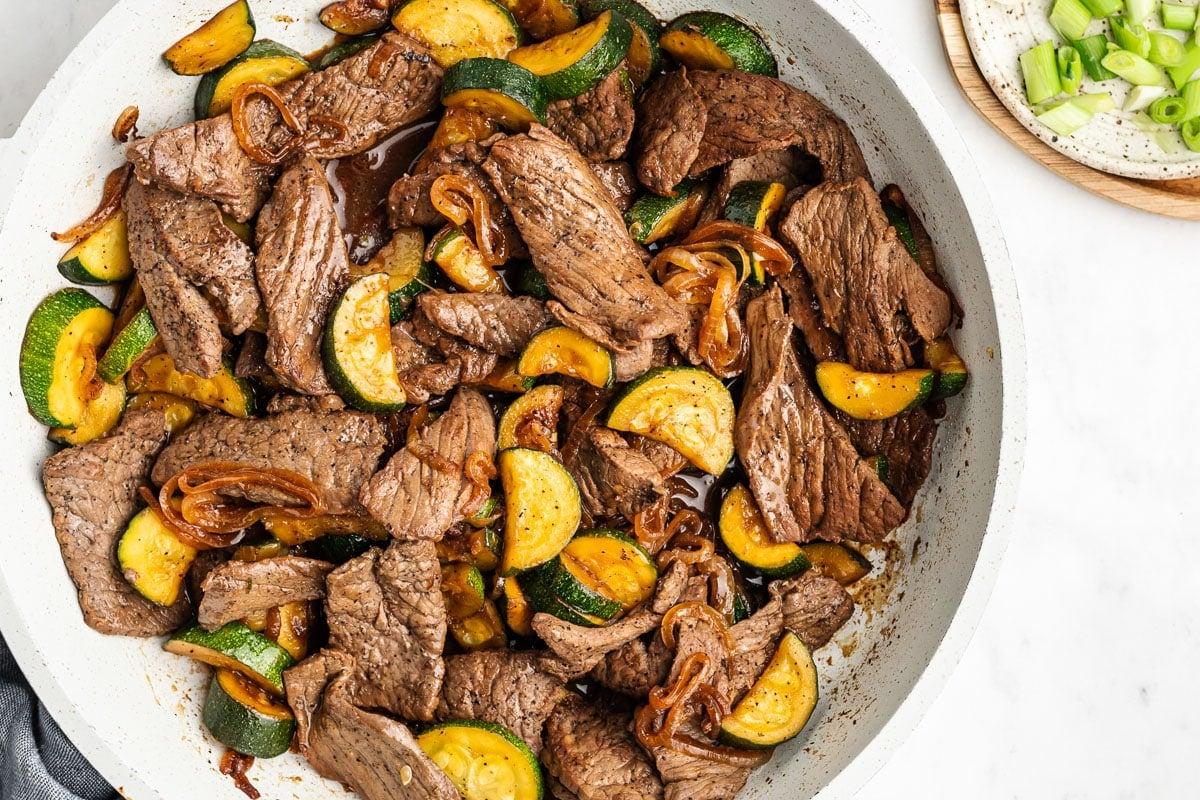 Steak-Zucchini-Pfanne 5 Eine Portion des Pfannengerichts auf Reis, garniert mit Frühlingszwiebeln und Sesamsamen.