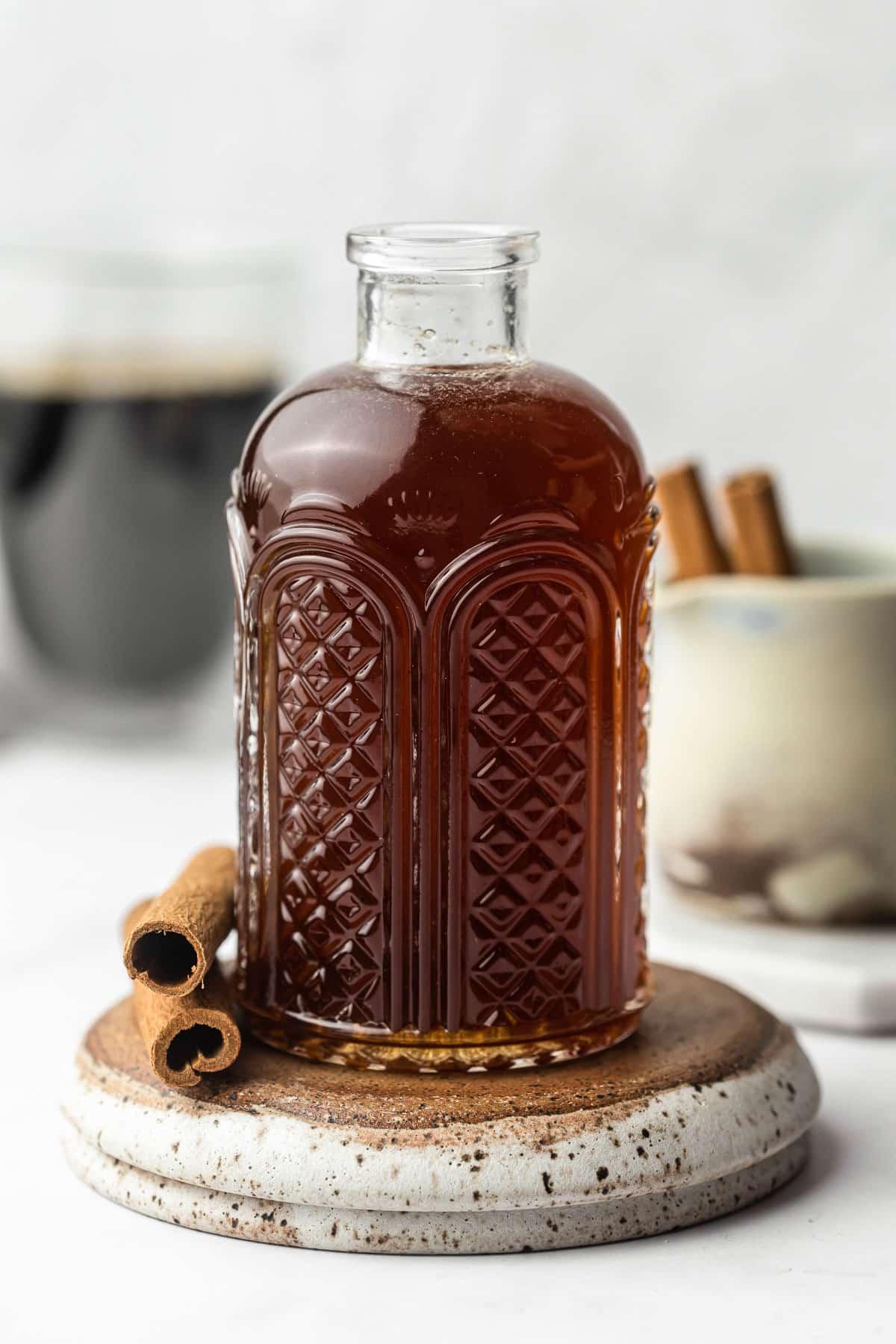 Ahorn-Zimt-Zuckersirup 5 Eine Nahaufnahme von Ahorn-Zimt-Sirup, der aus einer Karaffe in ein Glas fließt