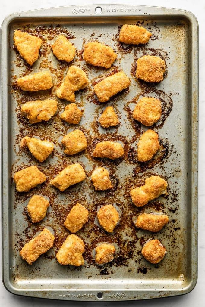 Gebackene Mandel-Hähnchen-Nuggets 5 Fertig gebackene Hähnchen-Nuggets mit Mandelmehl, serviert mit Honig-Senf-Dip und einer Beilage.