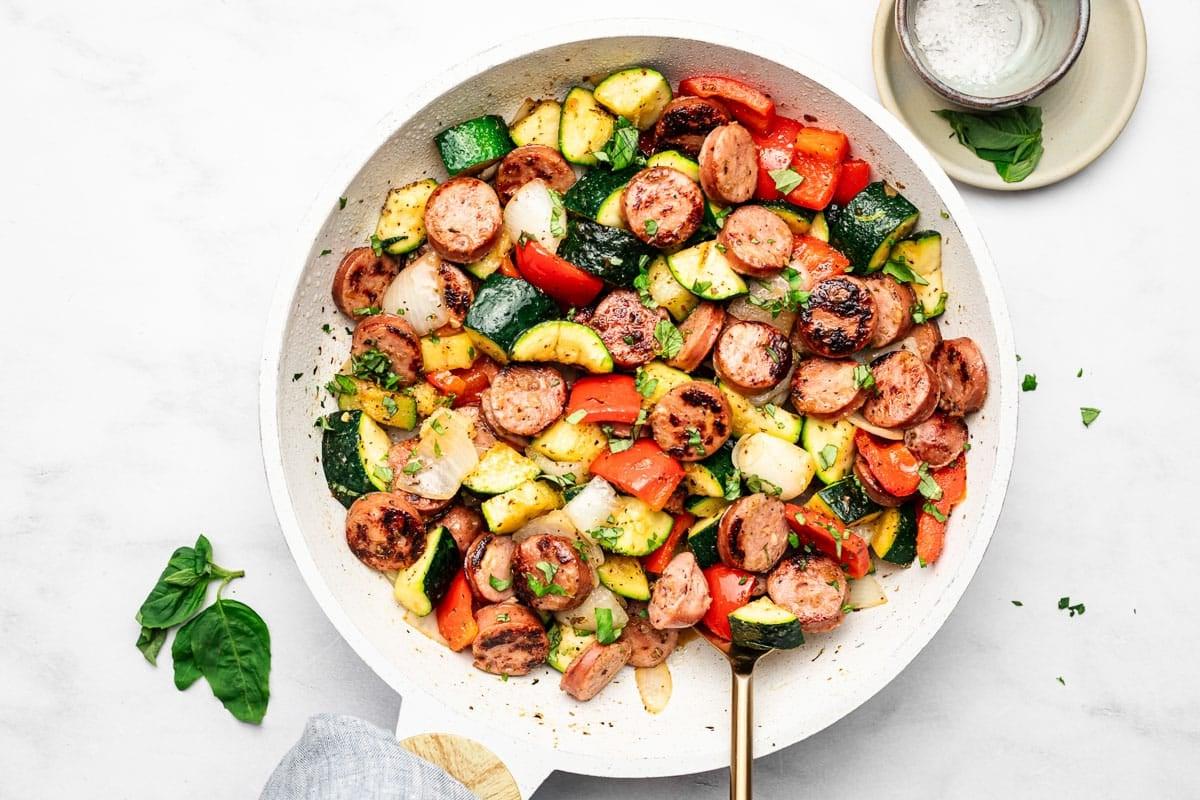 **20-Minuten-Wurst-Zucchini-Pfanne** 5 Ein Teller mit der fertig zubereiteten Zucchini-Wurst-Pfanne, bestreut mit frischen Kräutern.