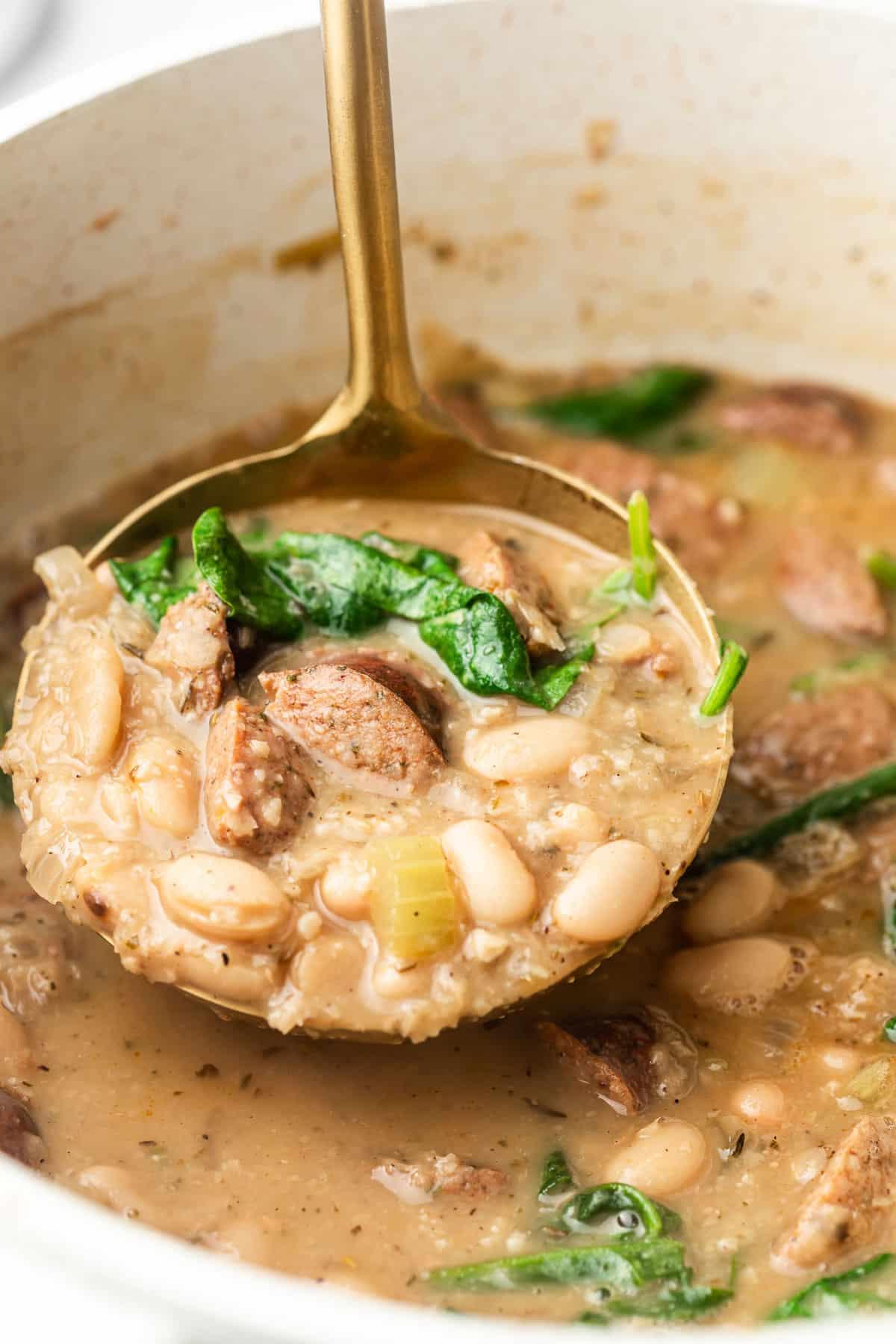 Einfache Wurst- und Weiße-Bohnen-Suppe 5 Eine dampfende Portion weiße Bohnensuppe mit Wurst, bereit zum Servieren, mit Brot und frischem Spinat daneben.