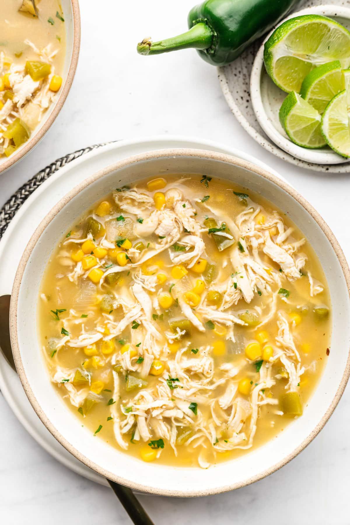 Nahaufnahme einer Schale Salsa Verde Hühnersuppe mit verschiedenen Garnierungen wie Avocado, Koriander und Limette.