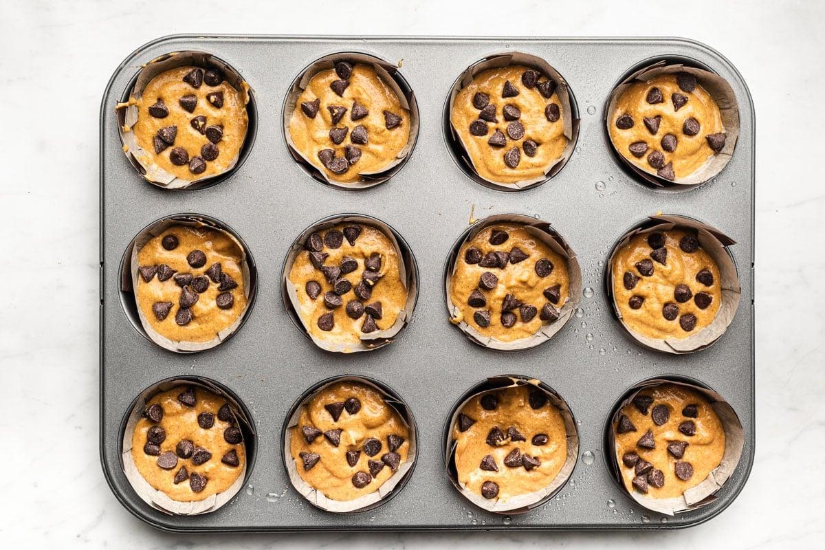 Eine Hand greift nach einem frisch gebackenen Kürbis-Haferflocken-Muffin aus der Muffinform