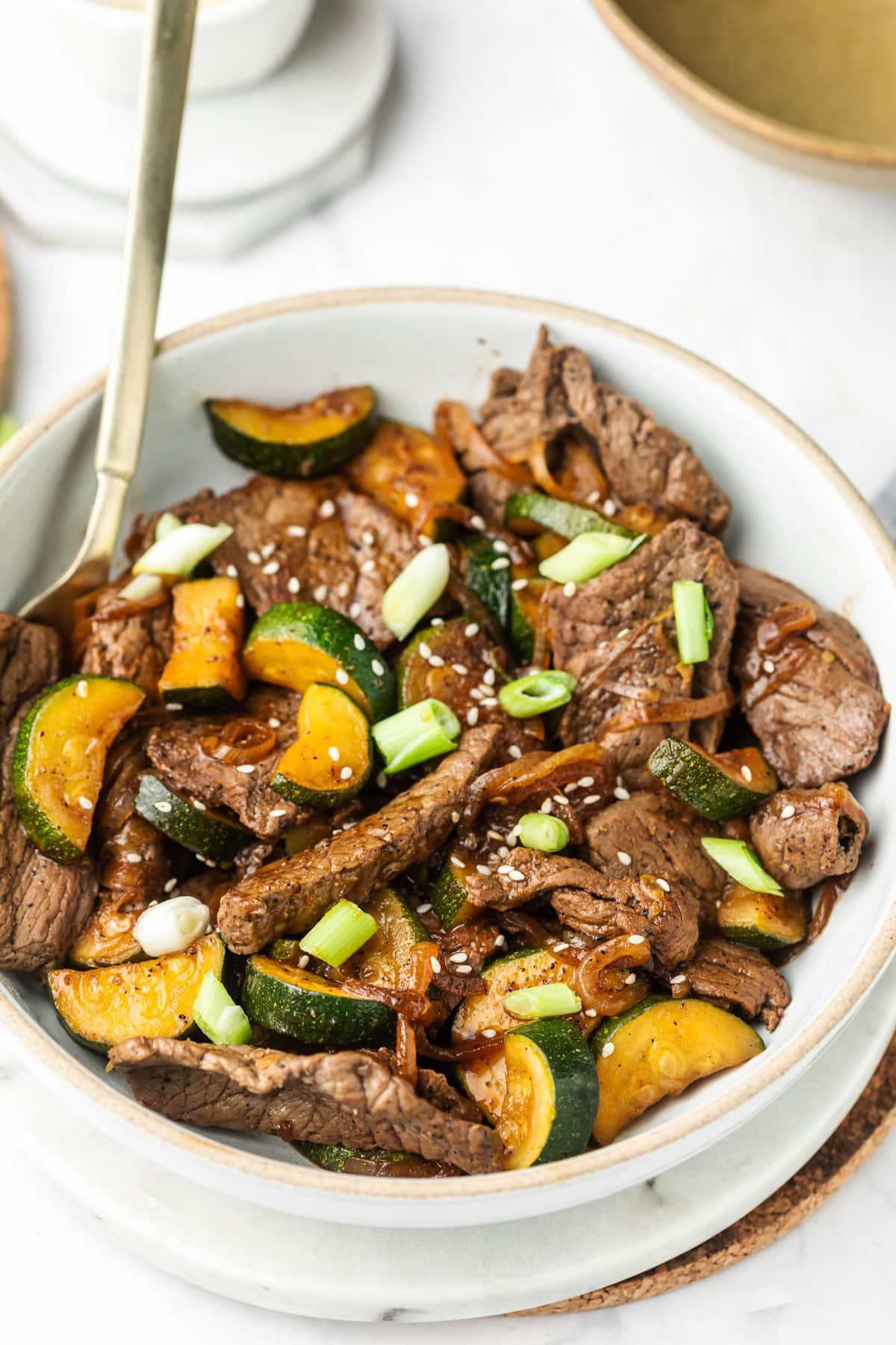 Steak-Zucchini-Pfanne 6 Eine Draufsicht auf das fertige Rindfleisch-Zucchini-Pfannengericht in einer Pfanne, mit einem Holzkochlöffel.