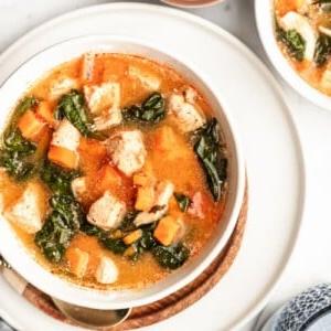 Eine Schüssel mit Instant Pot Buffalo Hähnchen Süßkartoffel Suppe, garniert mit frischen Kräutern.