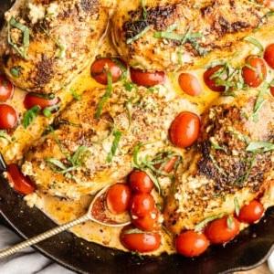 Hähnchen mit Feta-Sauce und Tomaten in einer gusseisernen Pfanne, angerichtet auf einem Holztisch.