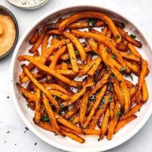 Tiefkühl-Süßkartoffel-Pommes aus der Heißluftfritteuse 7 Süßkartoffelpommes in einem Korb, daneben eine Schale mit Dip.