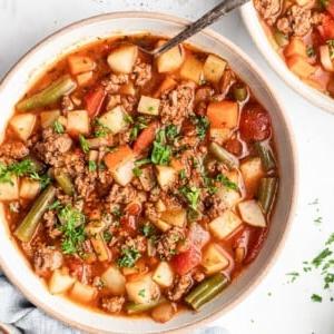 Gesunde 30-Minuten-Hamburger-Suppe 7 Ein Teller Hackfleischsuppe aus der Vogelperspektive, garniert mit frischer Petersilie, daneben ein Löffel.