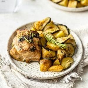 Blech-Hähnchen mit Kartoffeln und Zucchini 7 Fertig gebackenes Hähnchen vom Blech mit Kartoffeln und Zucchini auf einem Servierteller
