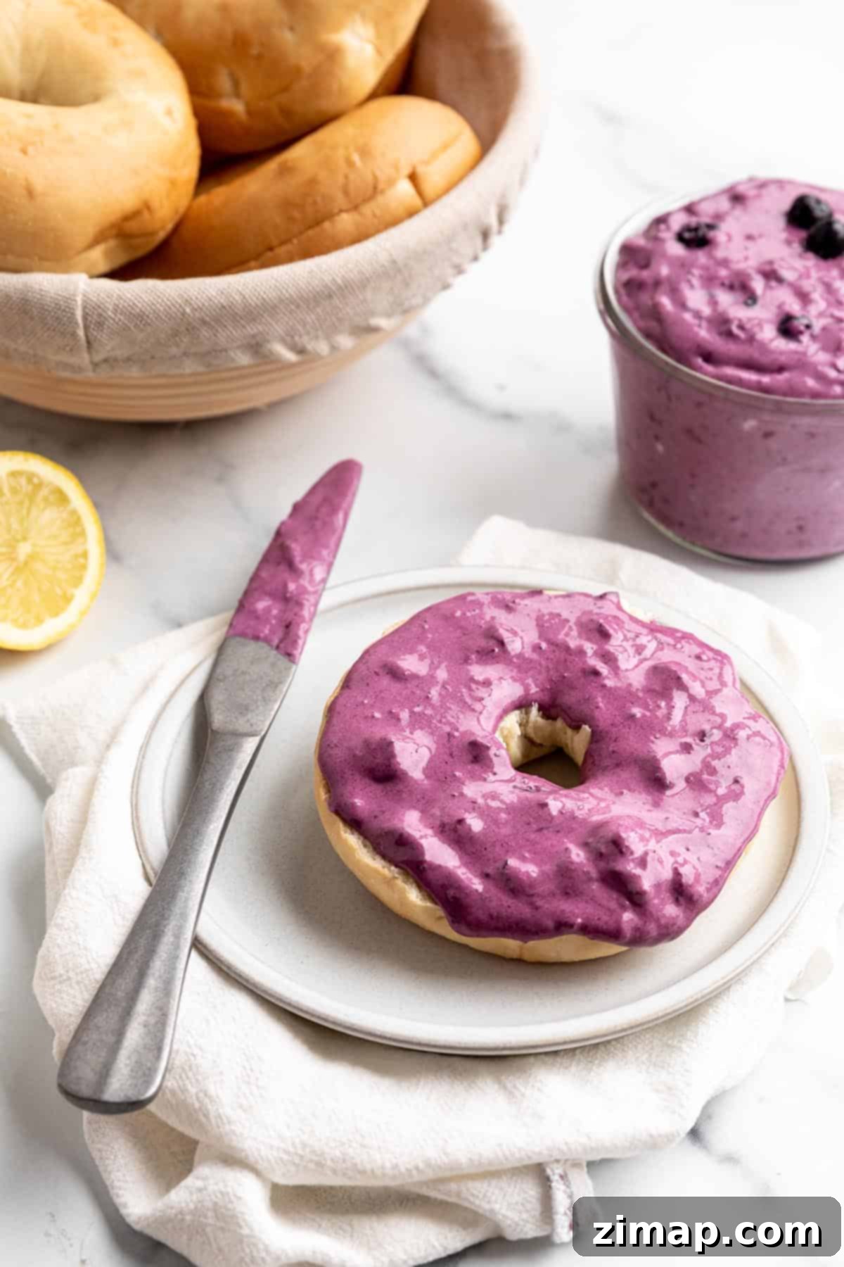 Μύρτιλο Τυρί Κρέμα 2 Ένα bagel με άλειμμα κρέμας τυριού μύρτιλου, καλάθι με bagels και ένα φρέσκο λεμόνι.
