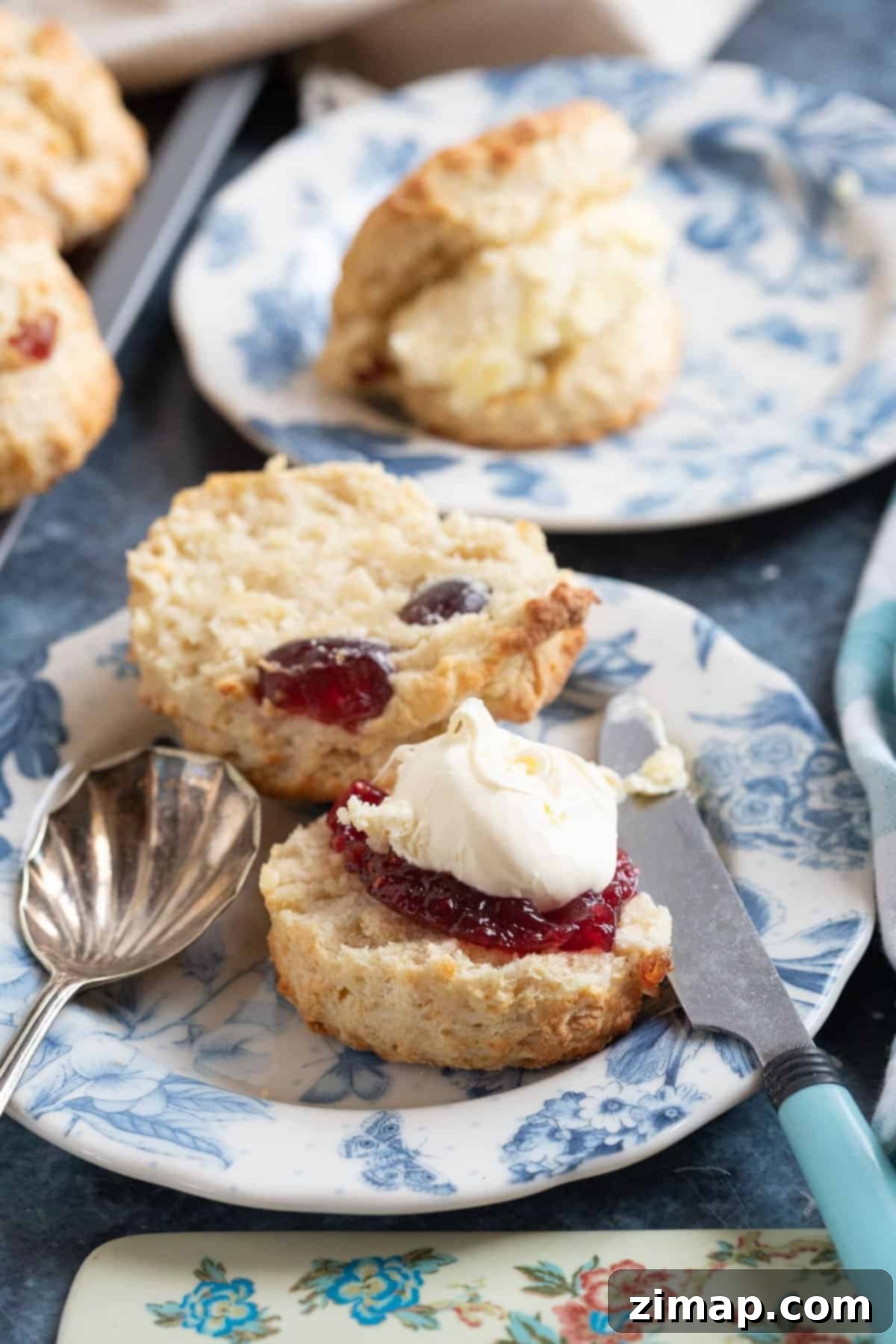 Αφράτα Γλυκάκια με Κεράσια και Αμύγδαλα 2 Scone με κεράσια και αμύγδαλα σε πιατάκι τσαγιού, σερβιρισμένο με μαρμελάδα και κρέμα πηγμένη.