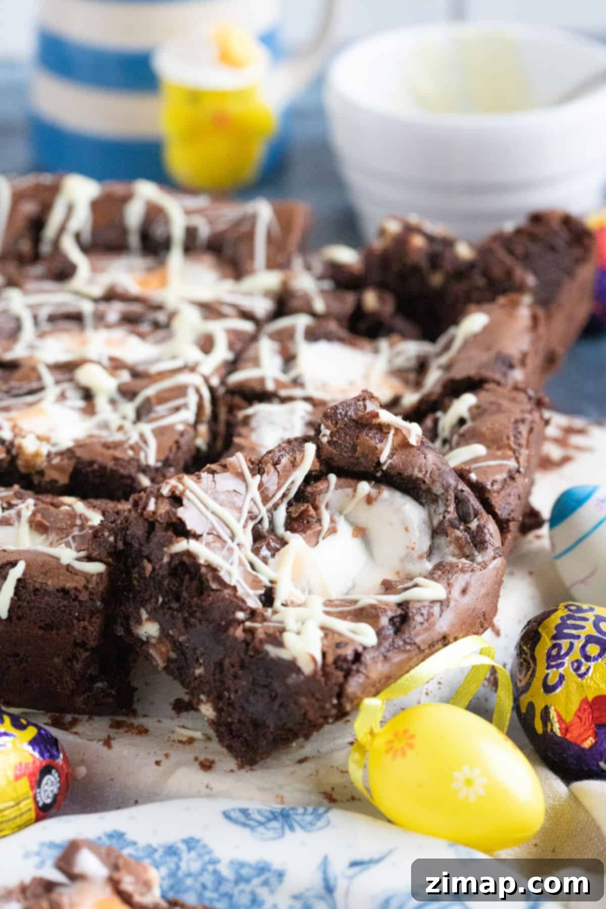 Εύκολα Μπράουνις με Αυγά Κρέμας Κάντμπερι 7 Creme egg brownies περιχυμένα με λευκή σοκολάτα σε ξύλινο δίσκο.