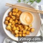 Τραγανό Τόφου Αέρος 9 Air fryer tofu cubes with a dipping sauce and chopsticks.