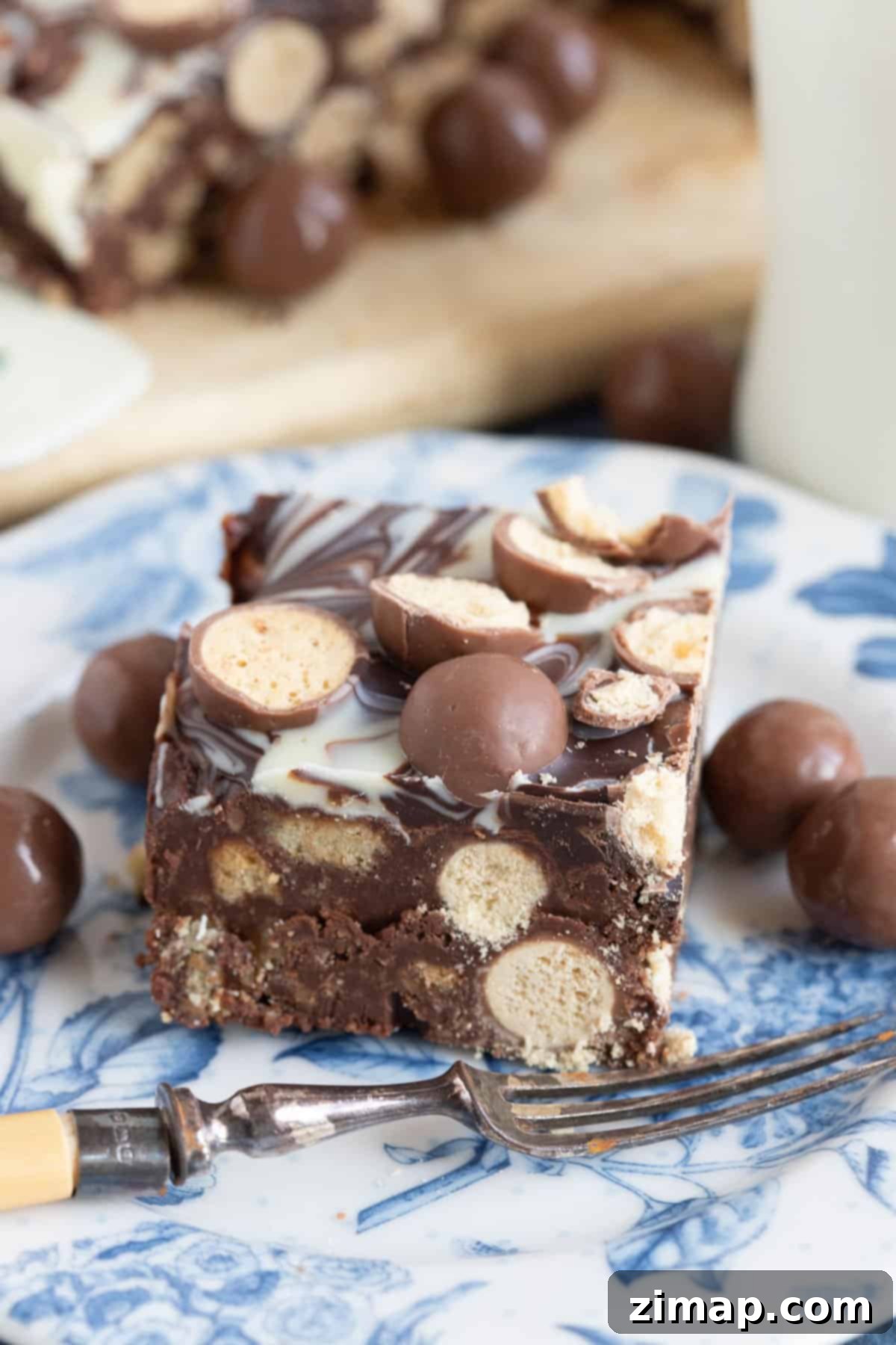 Το Αξεπέραστο Μπισκοτογλυκό Μαλτέζερ 4 A slice of Malteser tiffin on a blue and white plate.