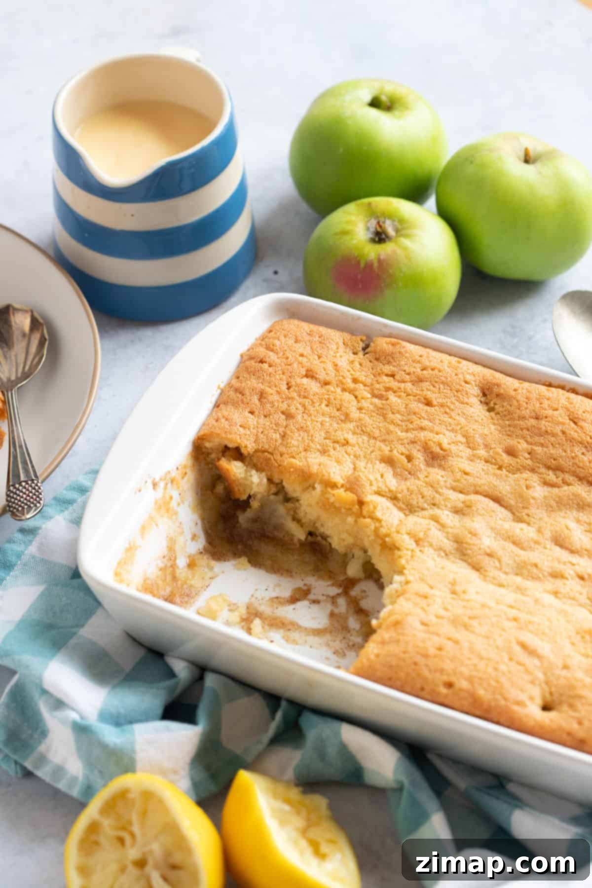 Εύκολη Πουτίγκα της Εύας 2 Eve's pudding σε λευκό ταψί με κανάτα με κρέμα κάσταρντ.