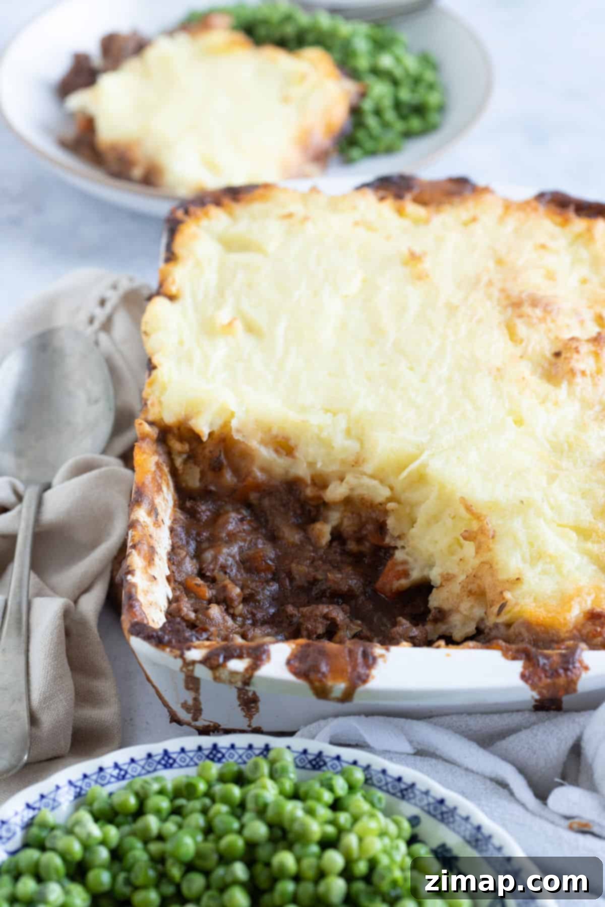 Πανεύκολο Κότατζ Πάι 8 Cottage pie σε λευκό πυρίμαχο σκεύος με ένα μπολ αρακά.