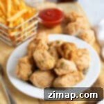 Σπιτικές Κοτομπουκιές Φριτέζας Αέρος 9 Τηγανητά νάγκετς κοτόπουλου σε λευκό πιάτο με πατάτες τηγανητές και κέτσαπ.