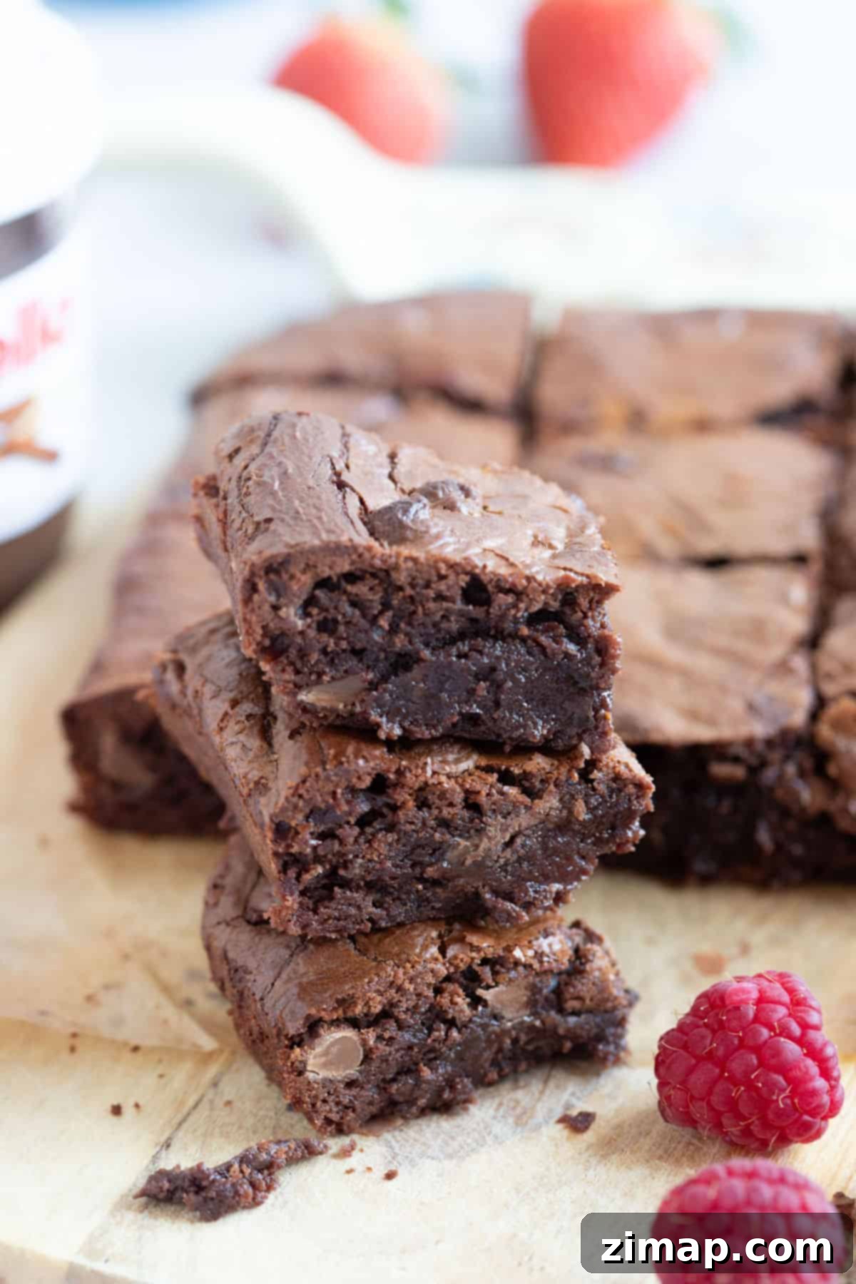 Μια στοίβα από brownies φτιαγμένα στη φριτέζα αέρος, τοποθετημένα σε ξύλινη σανίδα με φρέσκα σμέουρα δίπλα τους.