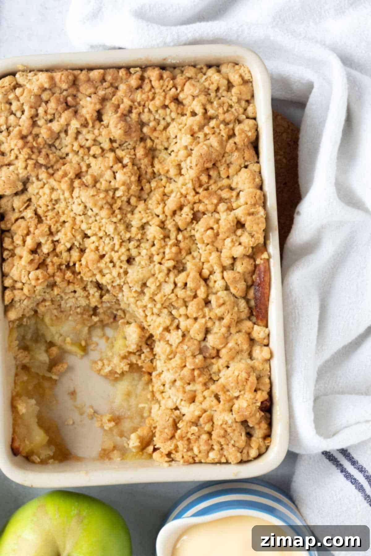 Εύκολο Κράμπλ Μήλου στο Air Fryer 11 Apple crumble σε ορθογώνιο ταψί με μια κανάτα κρέμας κάσταρντ.