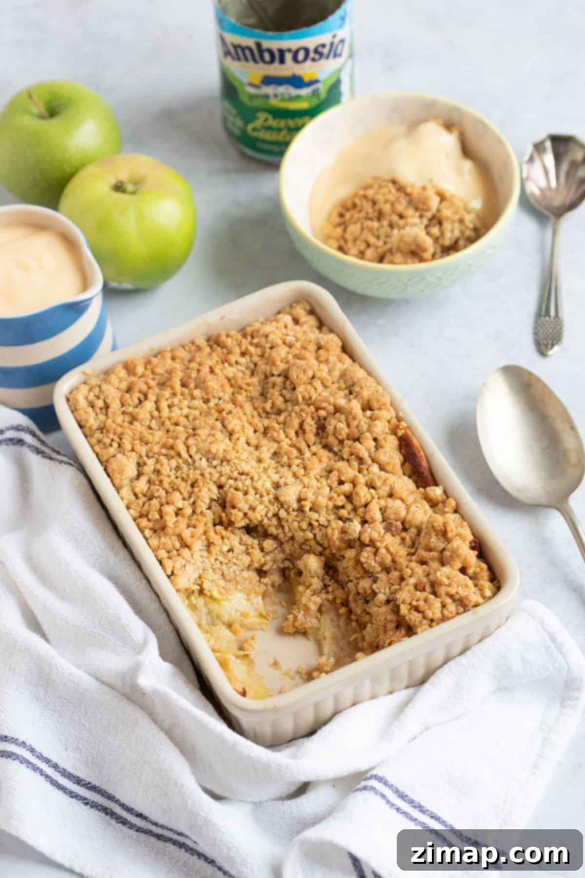 Εύκολο Κράμπλ Μήλου στο Air Fryer 9 Apple crumble σε φριτέζα αέρος σε ένα ταψί με μια κανάτα κρέμας κάσταρντ.