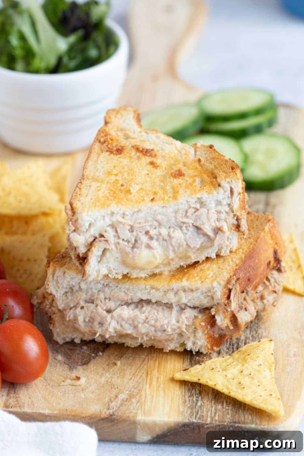 Η Απόλυτη Συνταγή Τόνου Melt για Φριτέζα Αέρος 11 Ένα σάντουιτς tuna melt από air fryer κομμένο στη μέση και σερβιρισμένο με πατατάκια τορτίγιας και ντομάτες.