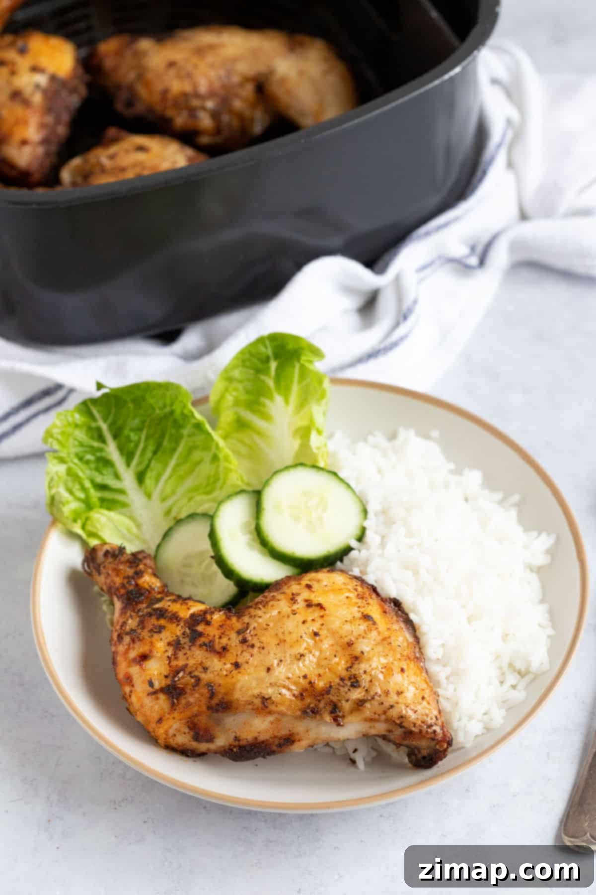 Αερόφρυτα Τραγανά Μπούτια Κοτόπουλου 7 A crispy air fryer chicken leg on a plate with rice and salad.