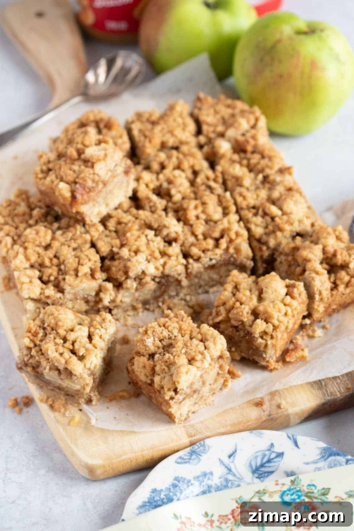 Μπάρες Μήλου και Biscoff Τριφτές 6 Μπάρες μήλου crumble σε πιατέλα παρουσίασης με μήλα στο φόντο.